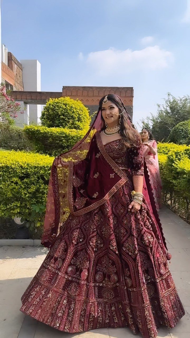 Bride in a wine-coloured lehenga photographed in the gardens at Fort JadhavGadh, Pune, bridal makeup and hair by Tejaswini Gote