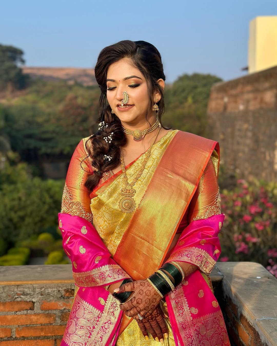 Maharashtrian bride in a gold Paithani saree and pink dupatta photographed on the ramparts at Fort JadhavGadh, Pune, bridal makeup, hair and draping by Tejaswini Gote