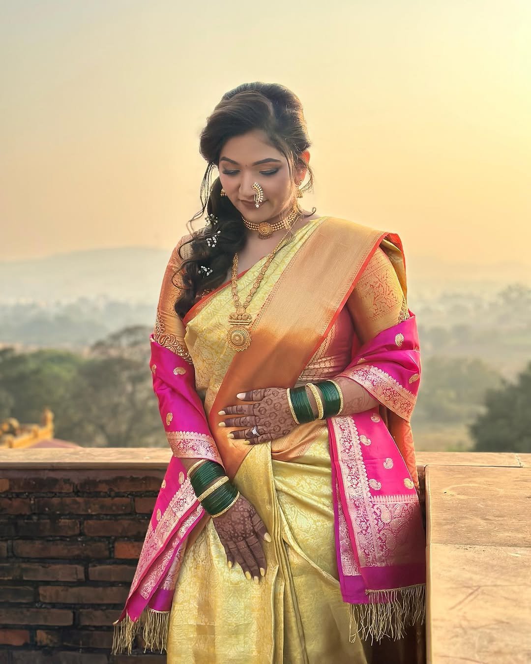 Bride in a gold Paithani saree in golden-hour light at Fort JadhavGadh, Pune, bridal makeup and hairstyling by Tejaswini Gote