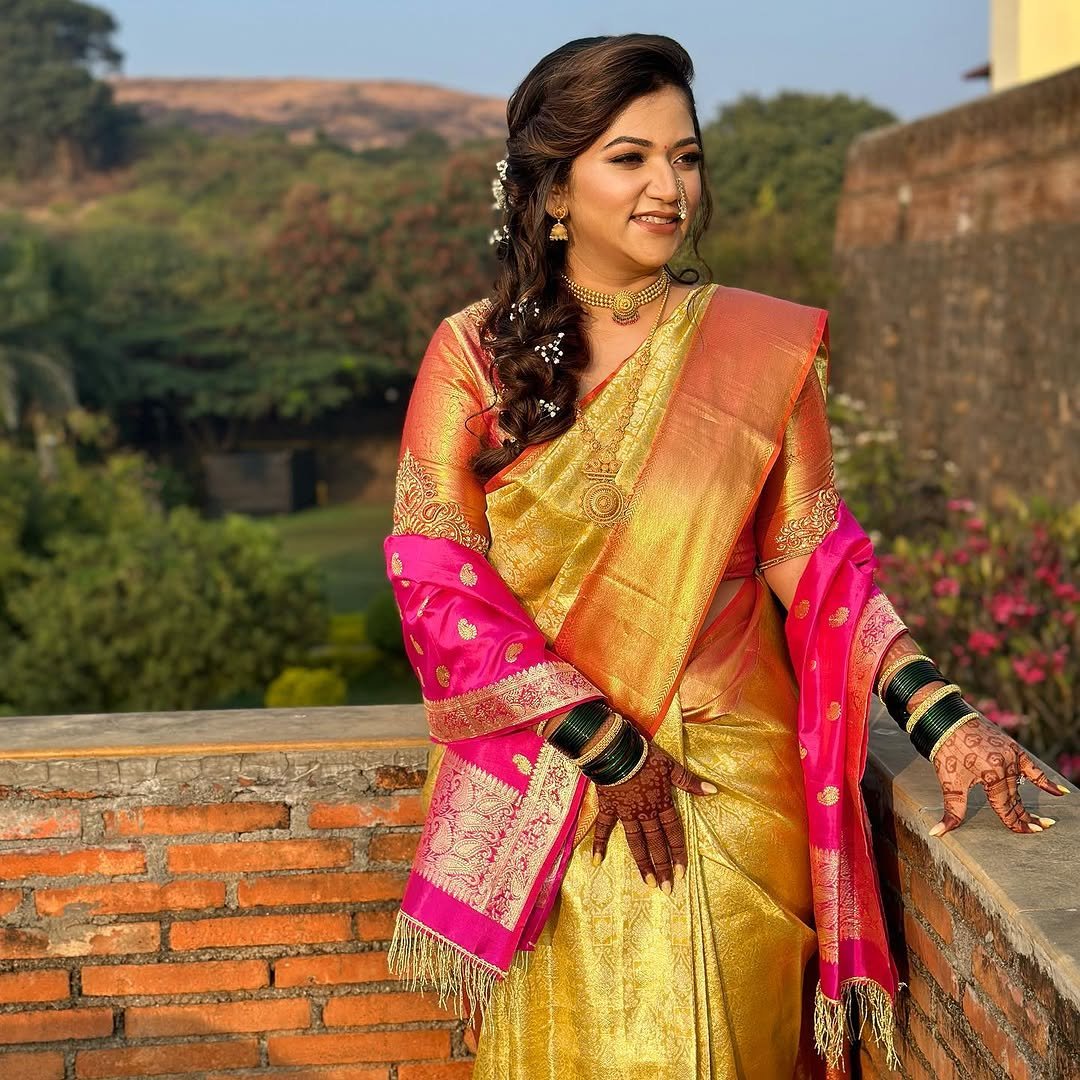 Bride in a gold and pink Paithani saree against the brick ramparts at Fort JadhavGadh, Pune, makeup by Tejaswini Gote