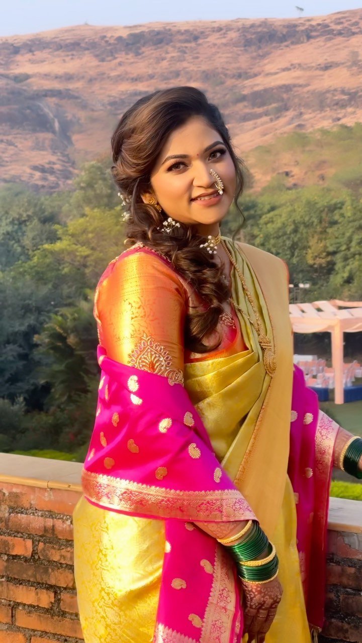 Bride in a gold and pink Paithani saree on the ramparts at Fort JadhavGadh with the Saswad hills behind her, makeup and hair by Tejaswini Gote